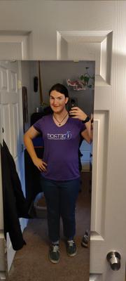 A woman takes a selfie in her bedroom mirror. She is wearing a purple t-shirt that reads 'i3Detroit Imagine, Innovate & Inspire' and blue jeans. Her dark hair is pulled back into a low ponytail.